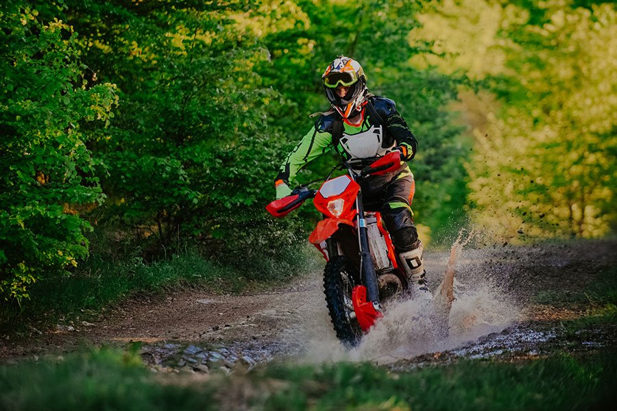 A man riding an enduro motorbike through a large puddle