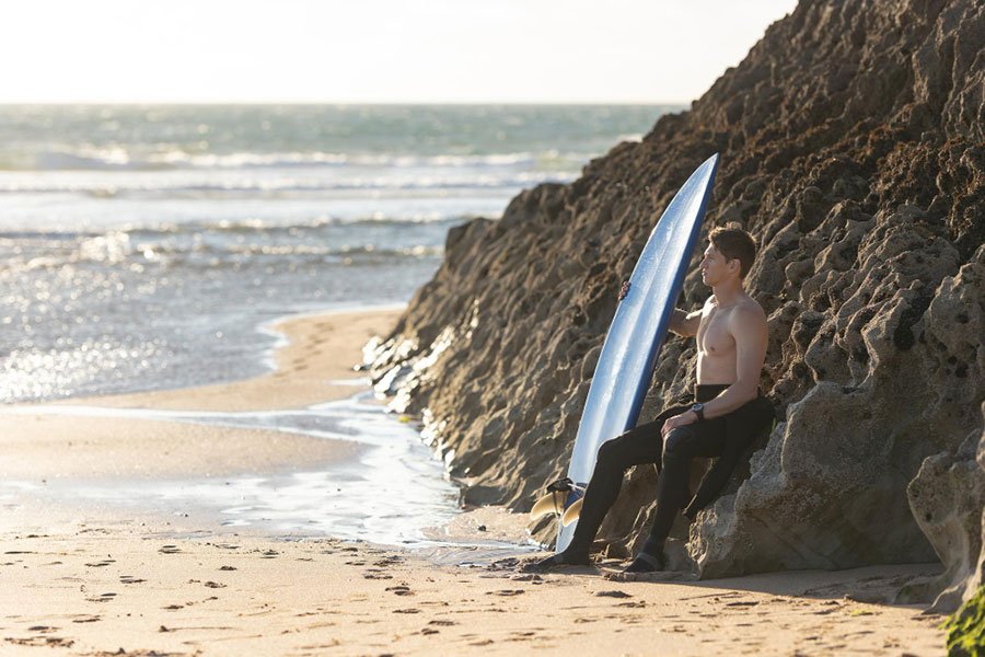 A man holding a surfboard, staring at the ocean