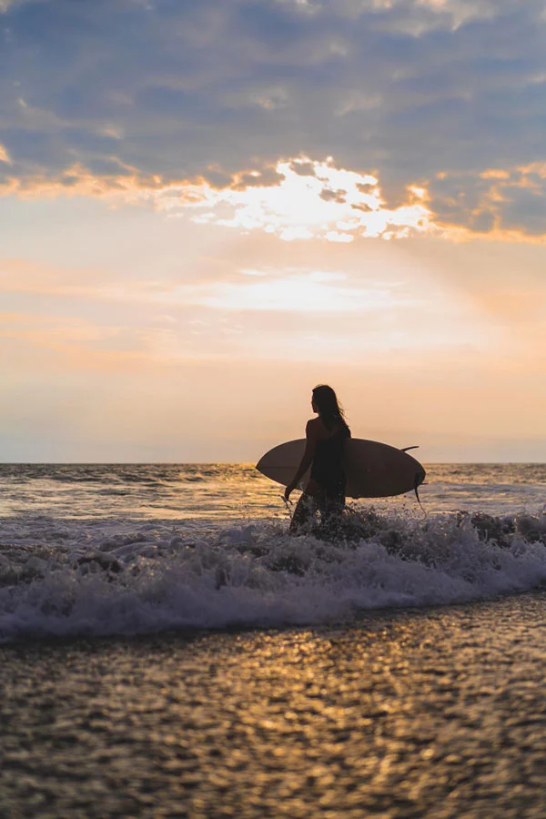 A woman holding a surfboard wading out to sea