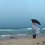 A woman standing on a beach in rainy weather
